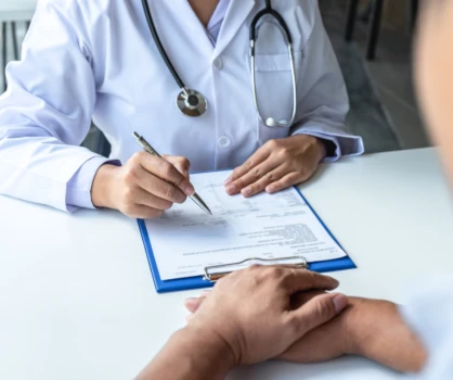 A doctor with a clipboard sitting across a desk from someone.