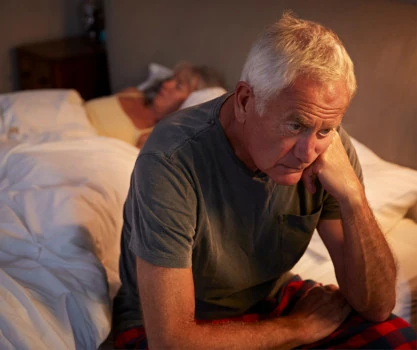 Man sitting on the edge of a bed, unable to sleep.